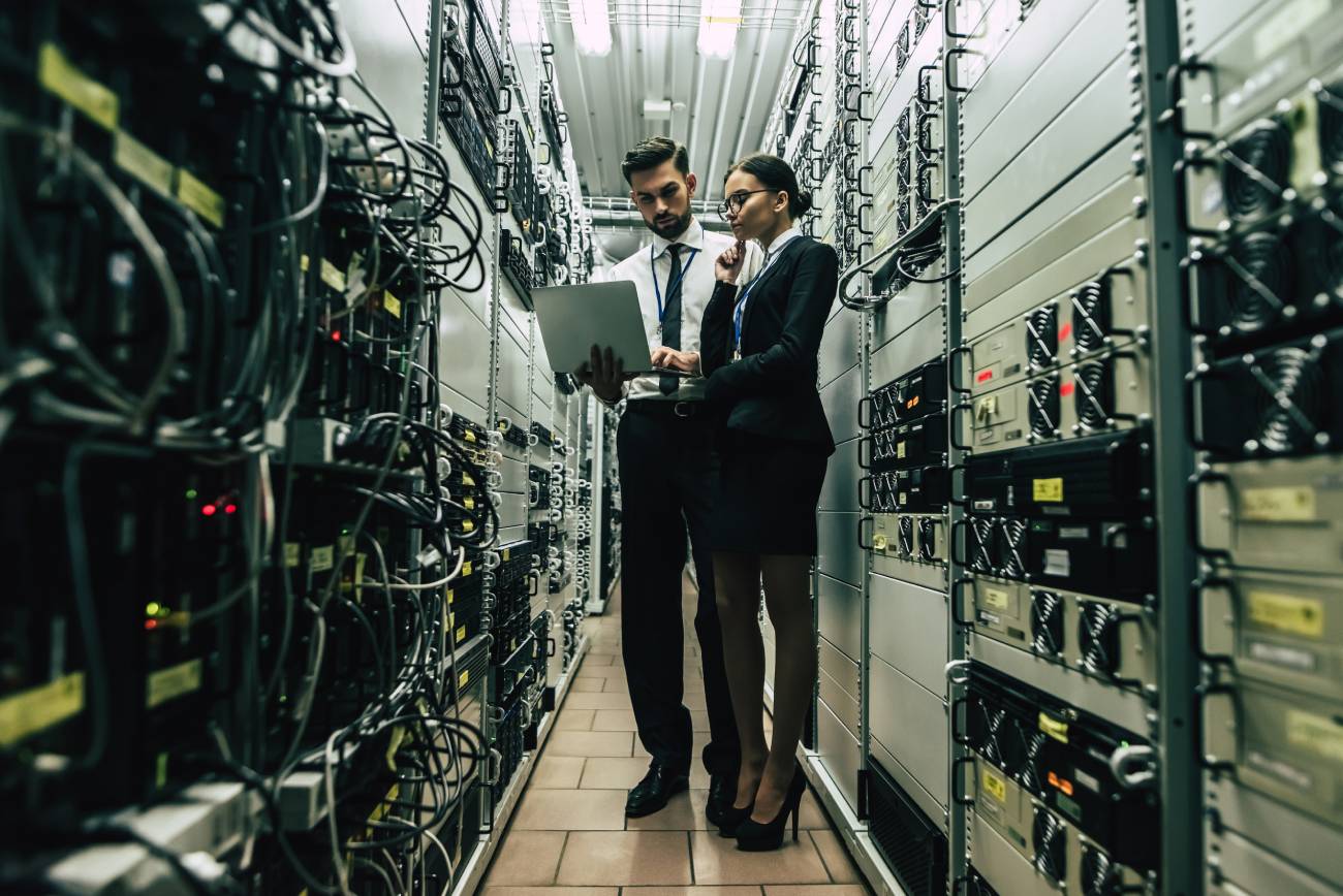 Male and Female IT Engineers in Network Server Room with Laptop